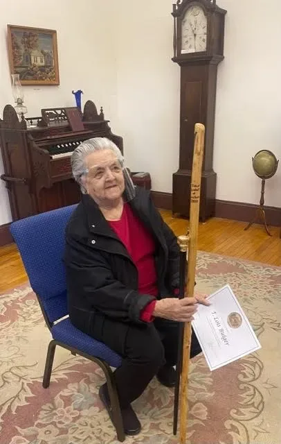 Portrait of Mrs. T. Lois Bulger seated with her walking stick and honoree certificate at the Vassalboro Historical Society