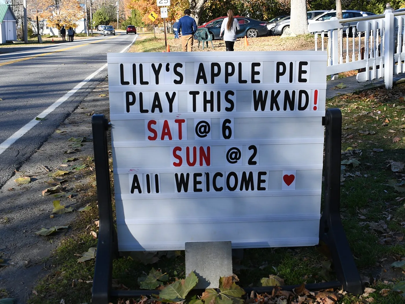 Hand-lettered roadside sign reading Lily's Apple Pie, play this wknd, Sat at 6, Sun at 2, all welcome