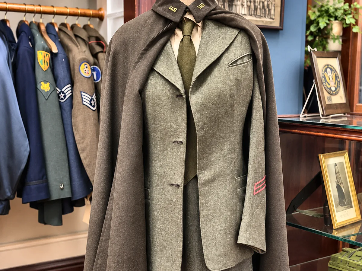 Marine Corps women&rsquo;s service uniform with a wool nurse&rsquo;s cape on a dress form, beside a rack of service uniforms