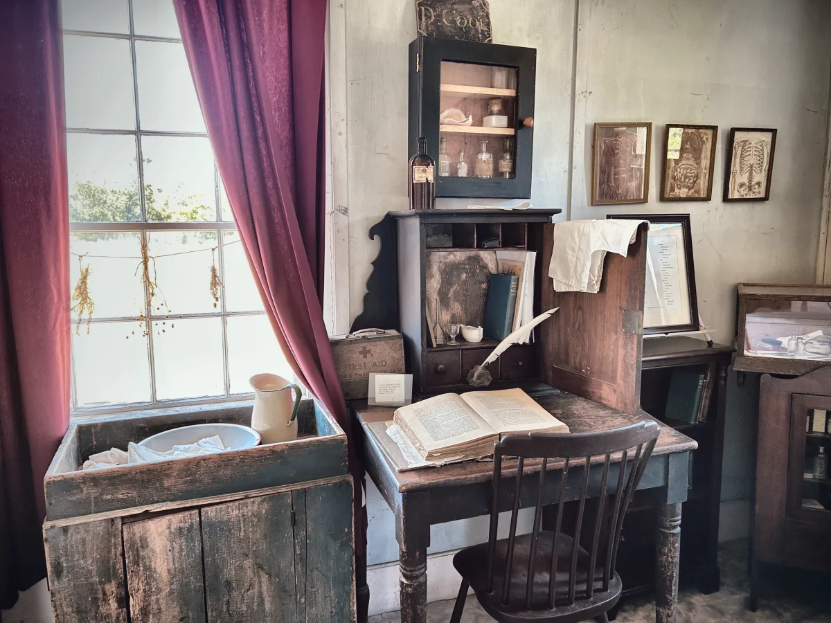 Doctor&rsquo;s office with washstand, desk, framed anatomical prints and a wall telephone