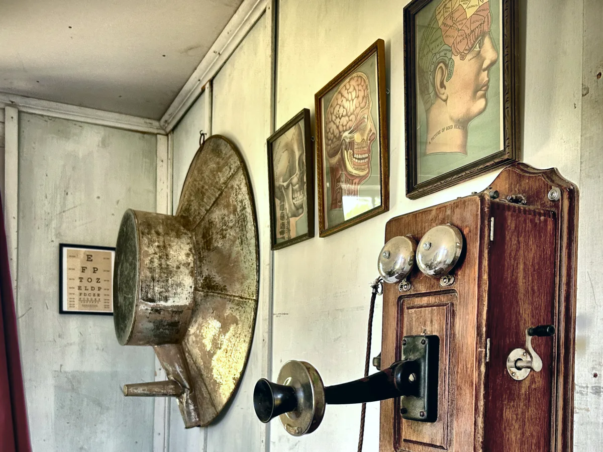 Oak crank wall telephone beside a stand up bathtub hung on the wall, an eye chart and framed anatomical prints