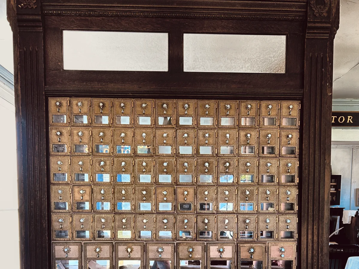 Tall oak post office box unit with rows of brass doors and glass windows