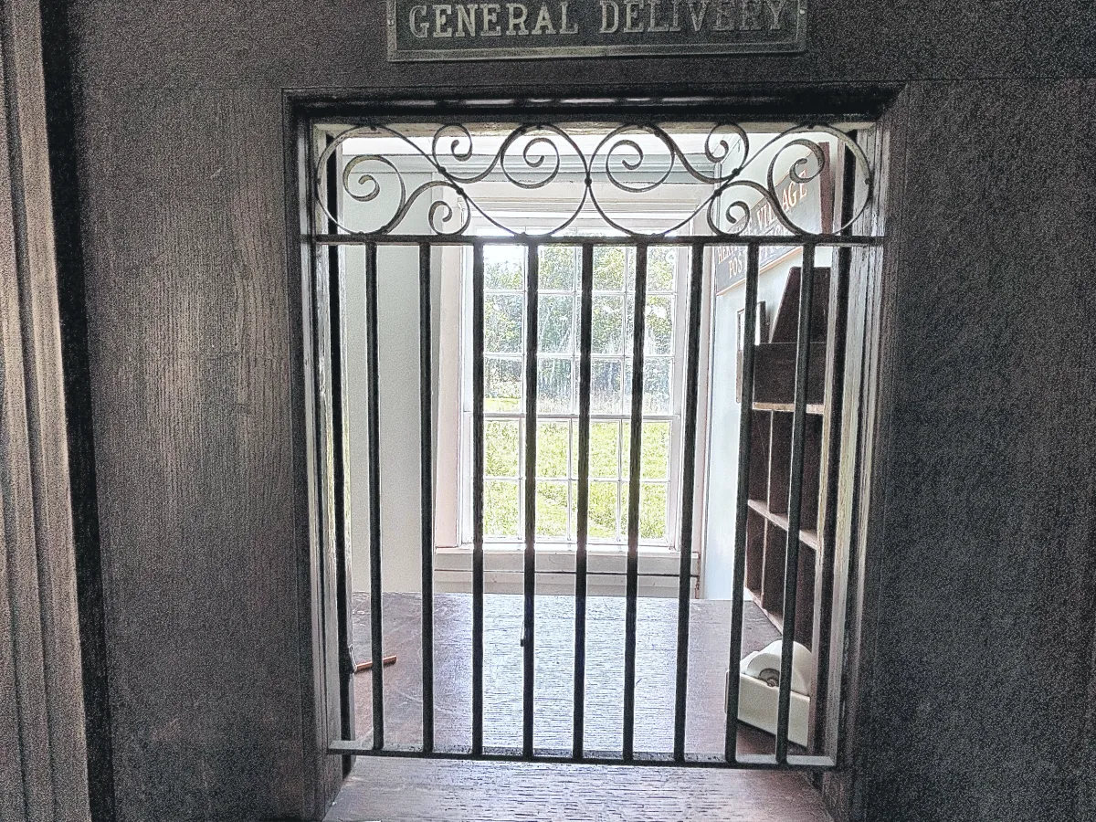 Post office service window with an iron grille beneath signs reading Stamps and General Delivery