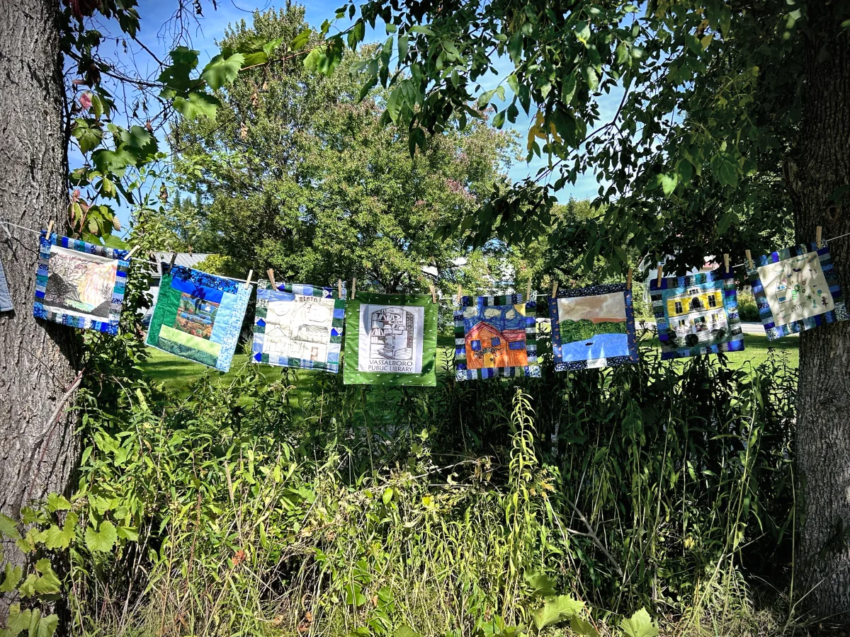 Quilt blocks on a clothesline including one showing the Vassalboro Public Library