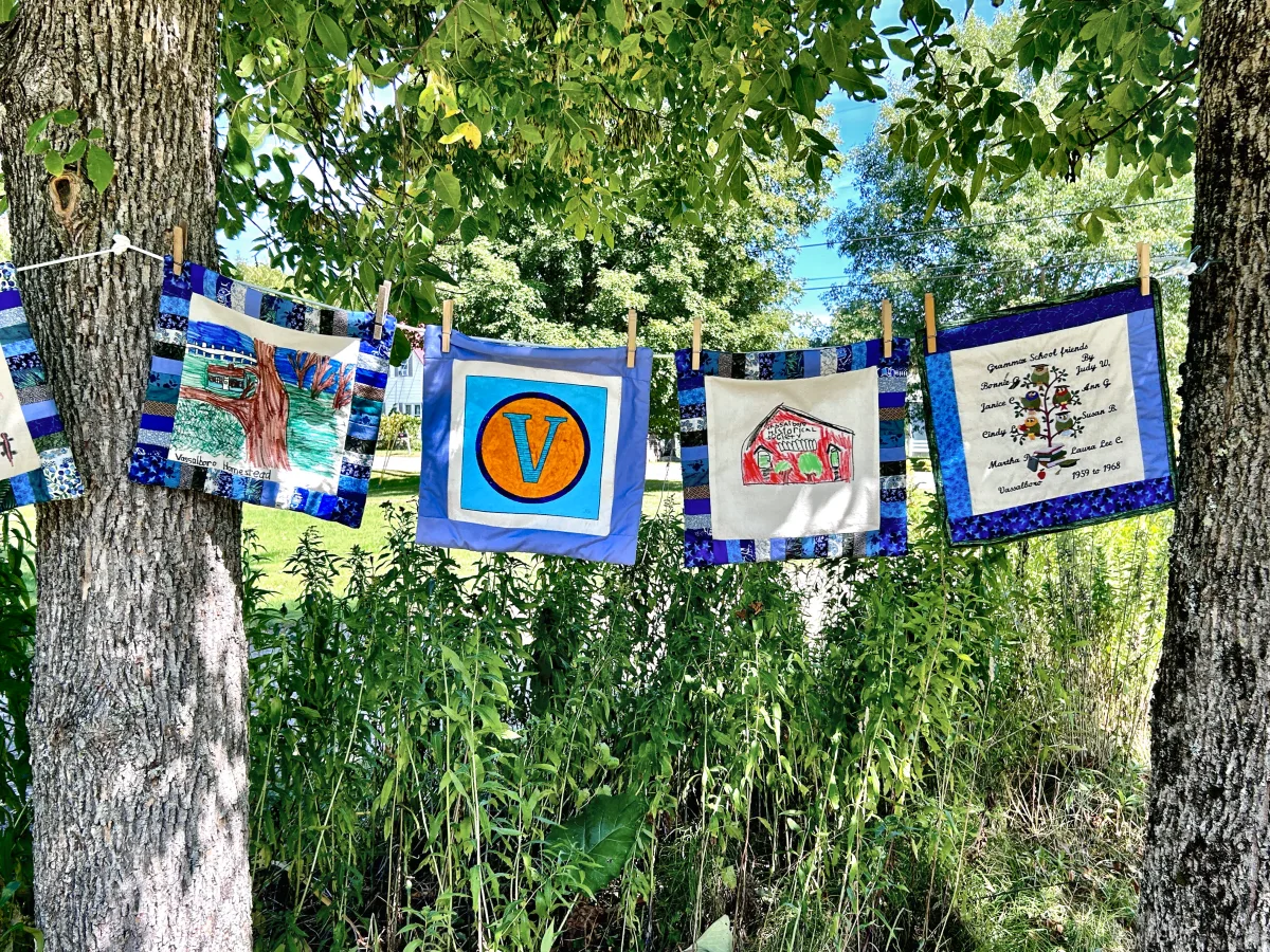 Community Quilt blocks pegged to a clothesline between two trees