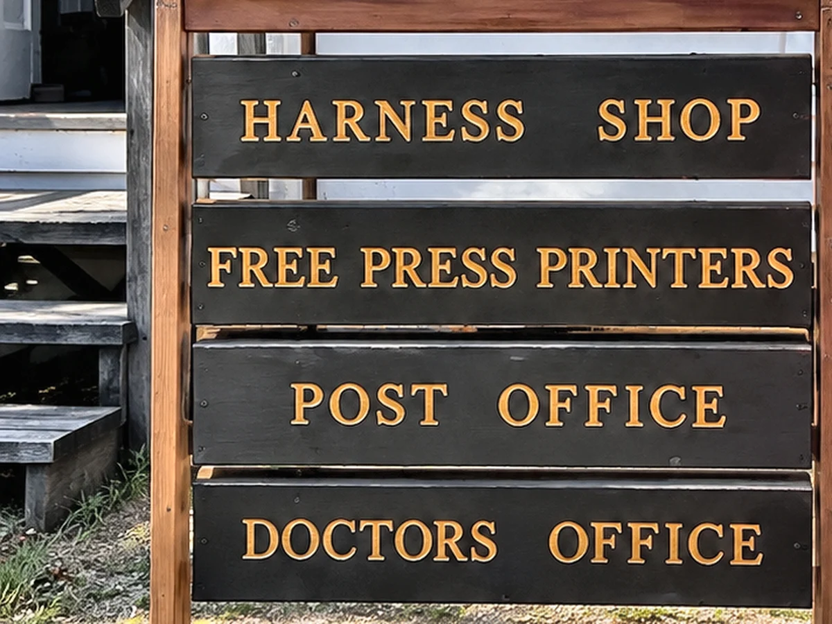 Painted Heritage Village sign board listing Harness Shop, Free Press Printers, Post Office and Doctors Office