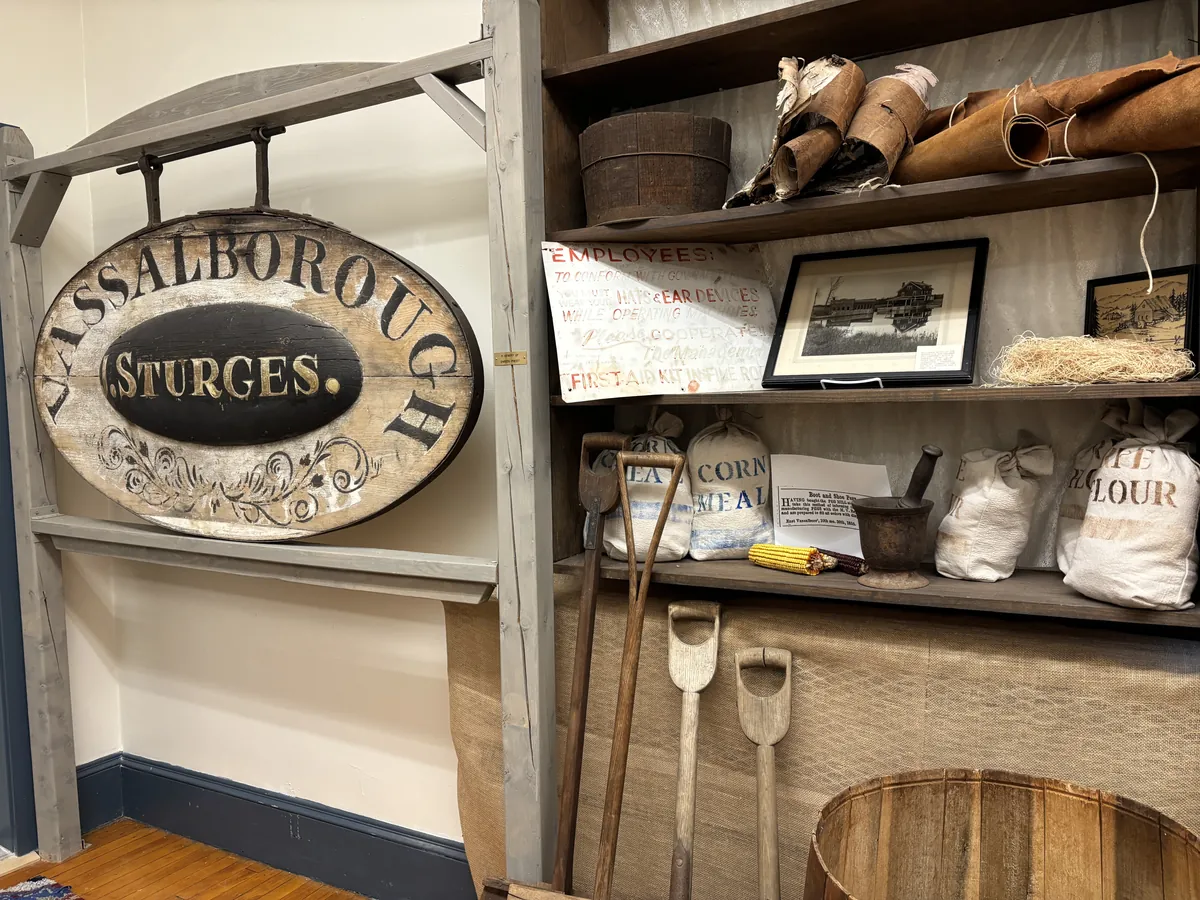 Original painted VASSALBOROUGH STURGES trade sign, next to mill safety notices, corn meal and rye flour sacks, and wooden farm tools