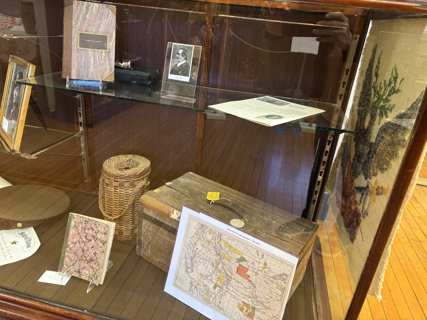 The John D. Lang display case: his personal ledger, a portrait of John D. Lang (1799-1879), an early map of Western United States Indian Reservations, a hand-woven basket, and a wooden document box