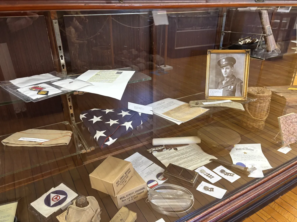 Display case with a framed portrait of PVT Harold V. Cox, a folded American flag, WWII combat rations, canteen, Purple Heart certificate, and service medals
