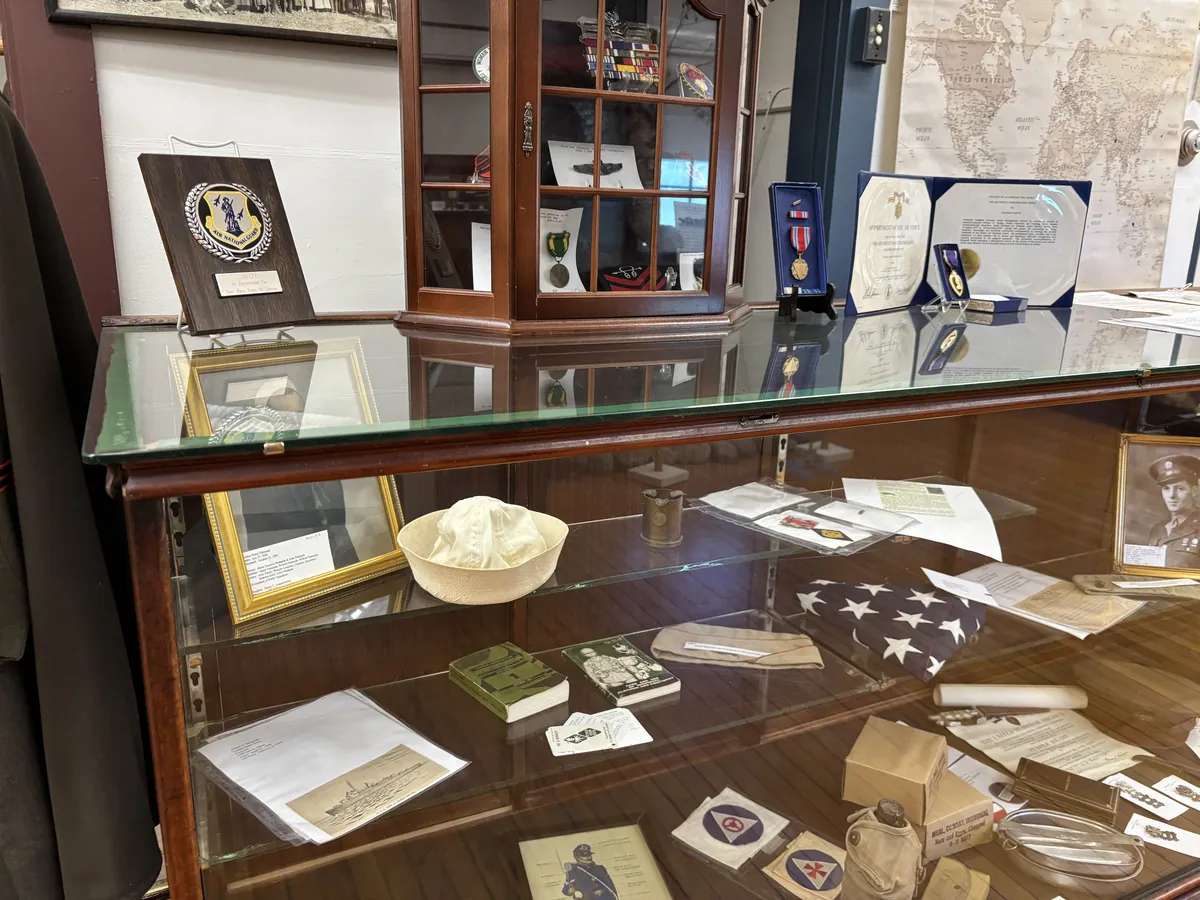 Display case with medals, Air National Guard plaque, sailor cap, framed portrait, and service commendations