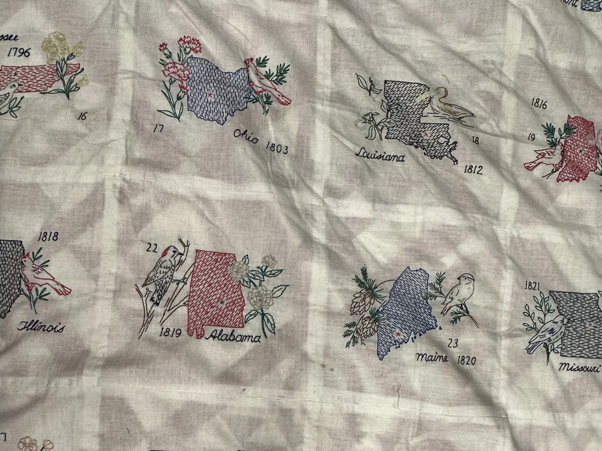 Embroidered state quilt with each state outlined in stitching beside its bird and flower, labelled with its name and the year it entered the Union